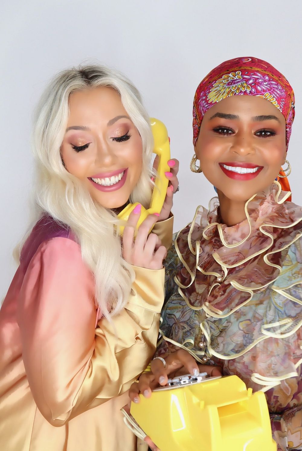 Two friends laugh into the yellow retro phone
