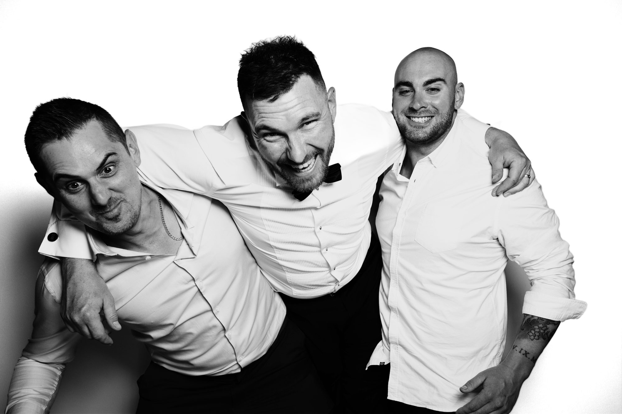 Black-and-white Glam Booth portrait: three groomsmen arm in arm, laughing