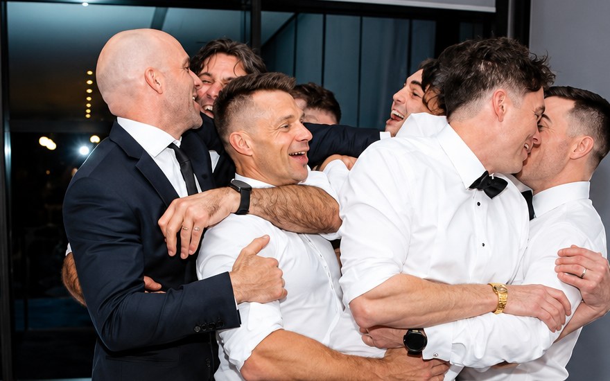 A group of men in suits hug and laugh