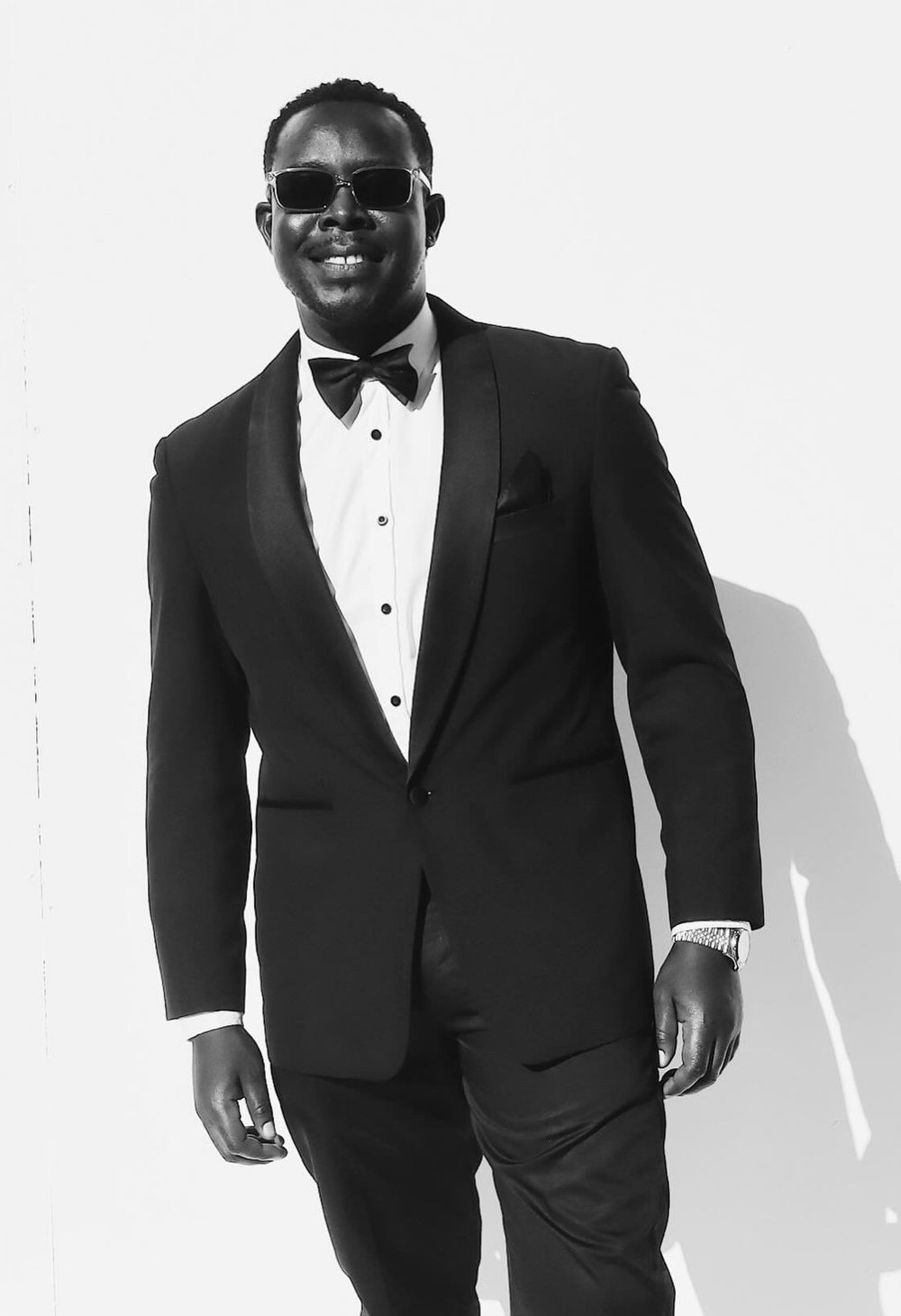 Black-and-white Glambot still: a man in a tux and sunglasses grins for the camera